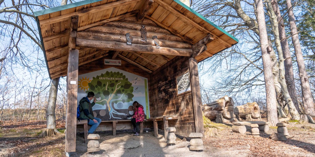 Auf dem Foto sitzen ein Jugendlicher und ein Mädchen in einer Holzhütte, in der eine Schautafel die Photosynthese kindgerecht erklärt., © Justine Bittner Auf dem Foto sitzen ein Jugendlicher und ein Mädchen in einer Holzhütte, in der eine Schautafel die Photosynthese kindgerecht erklärt., © Justine Bittner