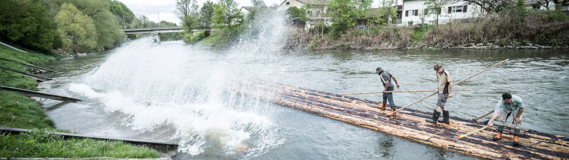 Flößer auf Stämmen im Wasser beim Floßbau, © Stadt Wolfratshausen, Adrian Greiter Flößer auf Stämmen im Wasser beim Floßbau, © Stadt Wolfratshausen, Adrian Greiter