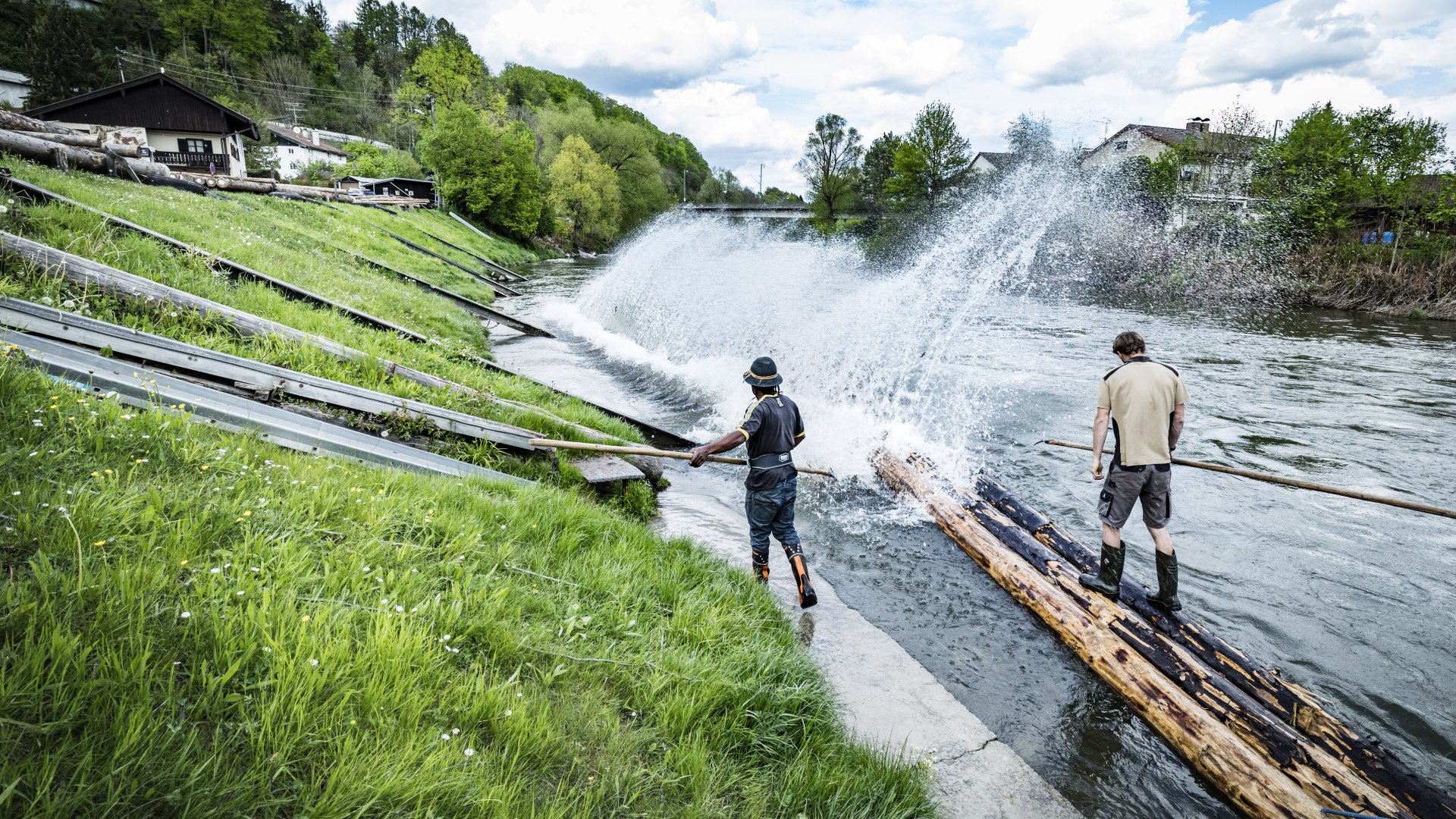 Zwei Männer stehen auf Baumstämmen und bauen ein Floß, © Stadt Wolfratshausen Foto: Adrian Greiter Zwei Männer stehen auf Baumstämmen und bauen ein Floß, © Stadt Wolfratshausen Foto: Adrian Greiter