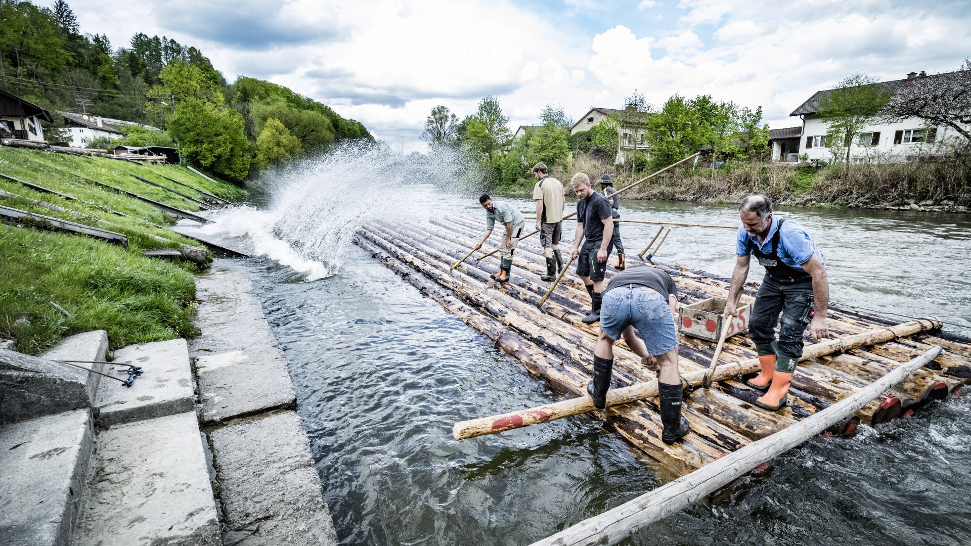 Das Bild zeigt Männer auf Stämmen im Wasser beim Bau eines Floßes. , © Stadt Wolfratshausen Foto: Adrian Greiter Das Bild zeigt Männer auf Stämmen im Wasser beim Bau eines Floßes. , © Stadt Wolfratshausen Foto: Adrian Greiter