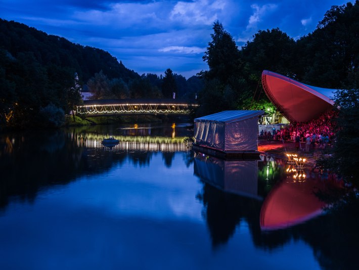 Die Loisach in der Abenddämmerung und die Bühne vom Fluss Festival, die bunt beleuchtet ist. Im Hintergrund der Sebastiani Steg., © Tom Hirschmann