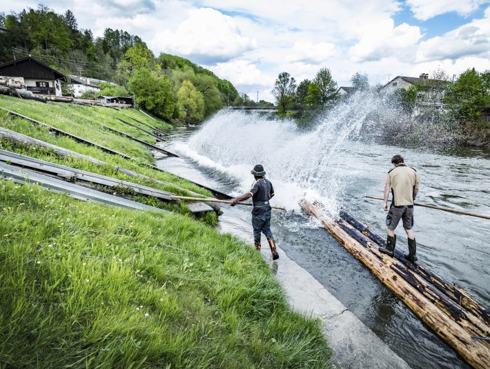 Zwei M&auml;nner stehen auf Baumst&auml;mmen und bauen ein Flo&szlig;, &copy; Stadt Wolfratshausen Foto: Adrian Greiter