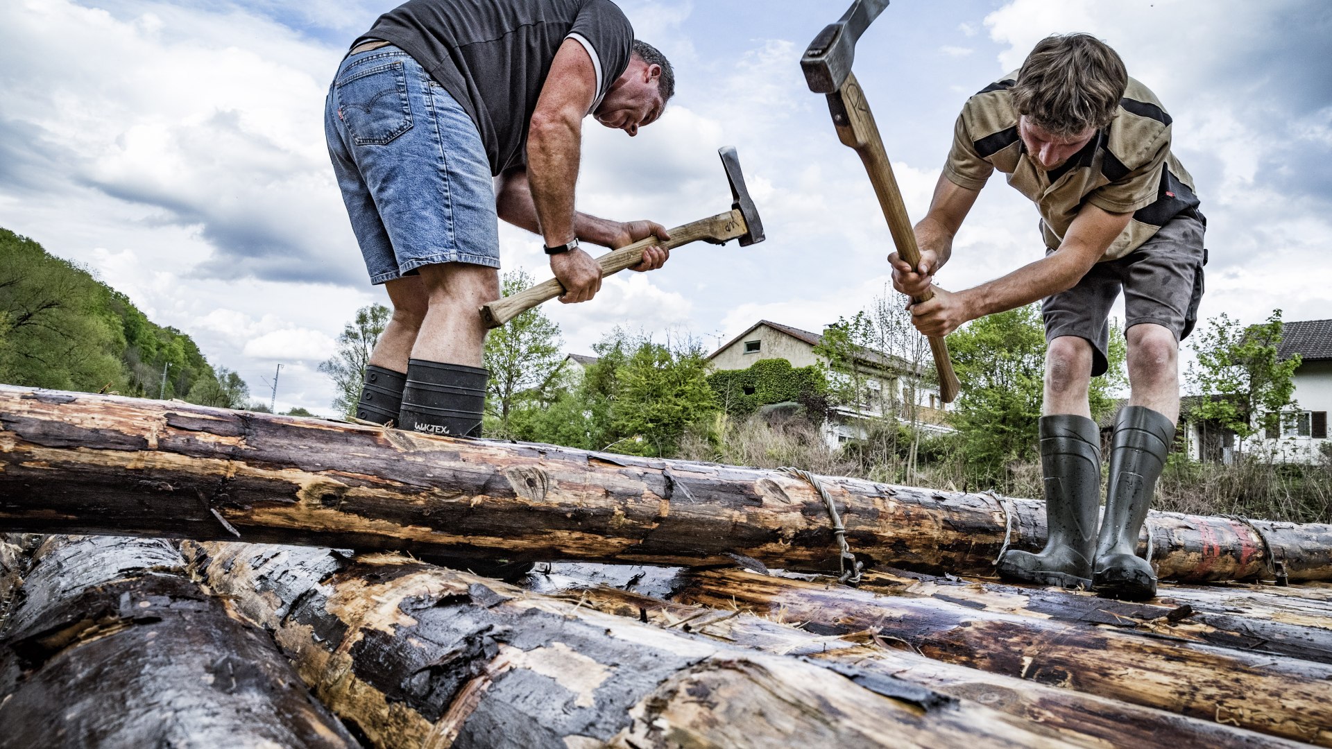 Zwei M&auml;nner bauen mit &Auml;xten Baumst&auml;mme zu einem Flo&szlig; zusammen, &copy; Stadt Wolfratshausen Foto: Adrian Greiter