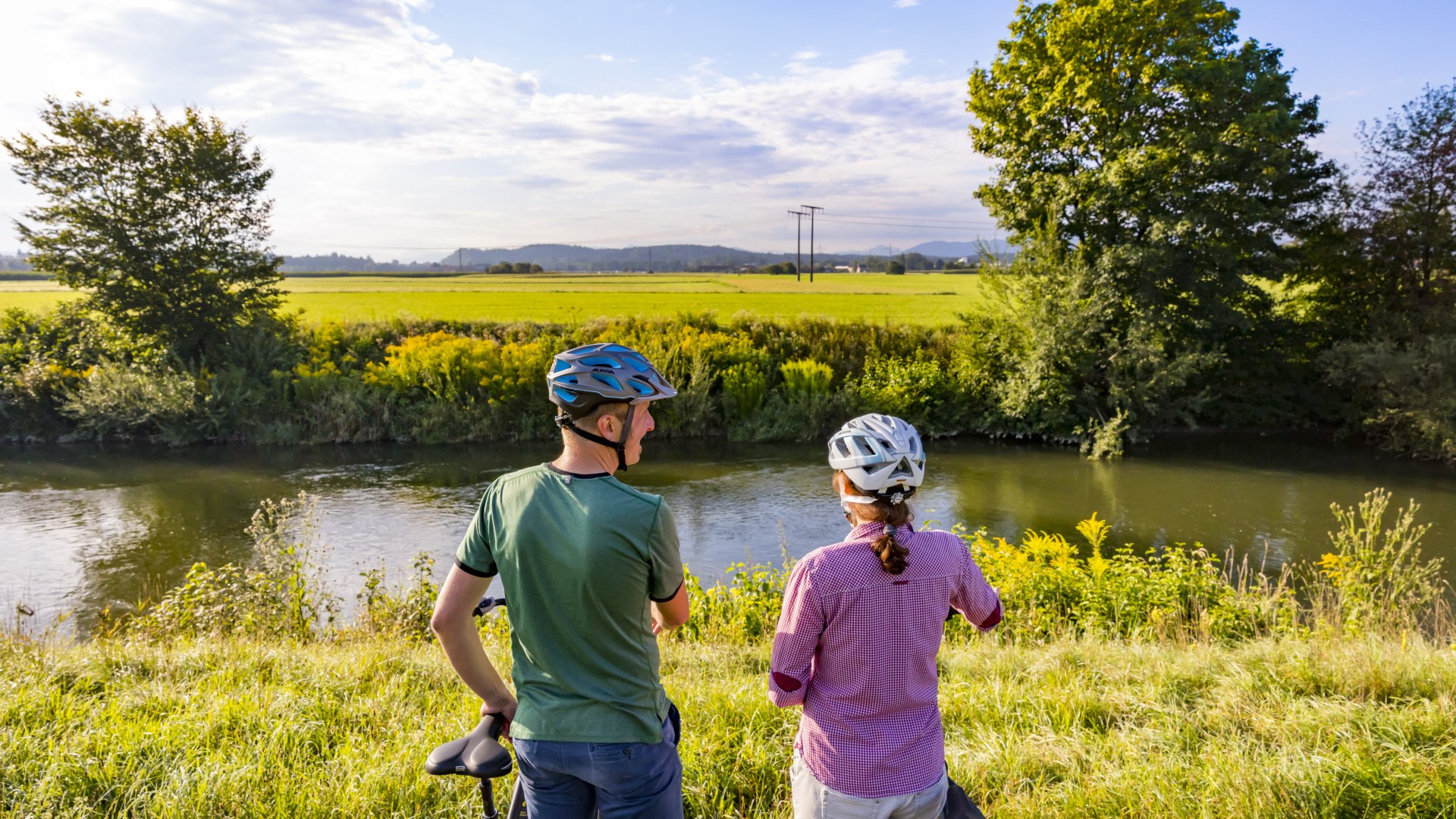 Ein Paar mit Fahrr&auml;dern steht am Isar Loisach Kanal und schaut auf&acute;s Wasser. , &copy; Stadt Wolfratshausen Foto: Adrian Greiter