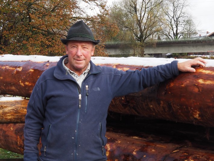 Josef Seitner mit Hut in Arbeitskleidung vor einem Stapel Baumst&auml;mme, die f&uuml;r ein Flo&szlig; bereit liegen. 