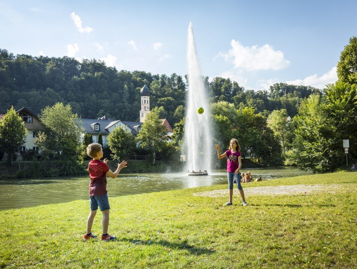 Zwei Kinder spielen auf einer Wiese vor der Fontäne an der Floßlände, © Adrian Greiter