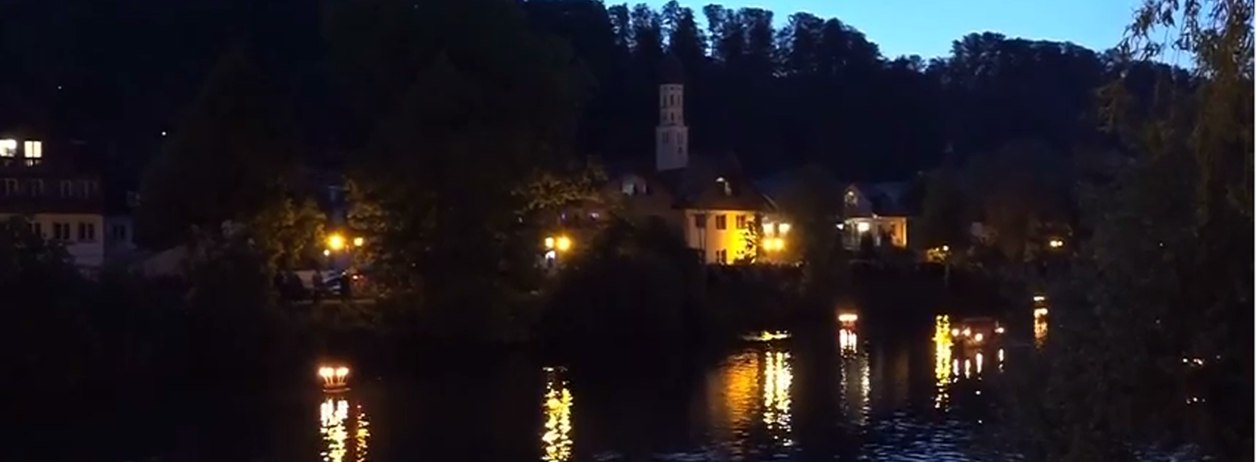 Die Loisach in der Abenddämmerung mit beleuchteten Häusern am gegenüberliegenden Ufer. 